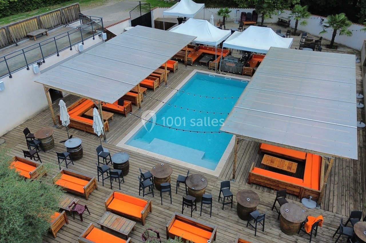 Vue aérienne d'une terrasse avec piscine centrale, entourée de tables, chaises et banquettes orange sous des pergolas.
