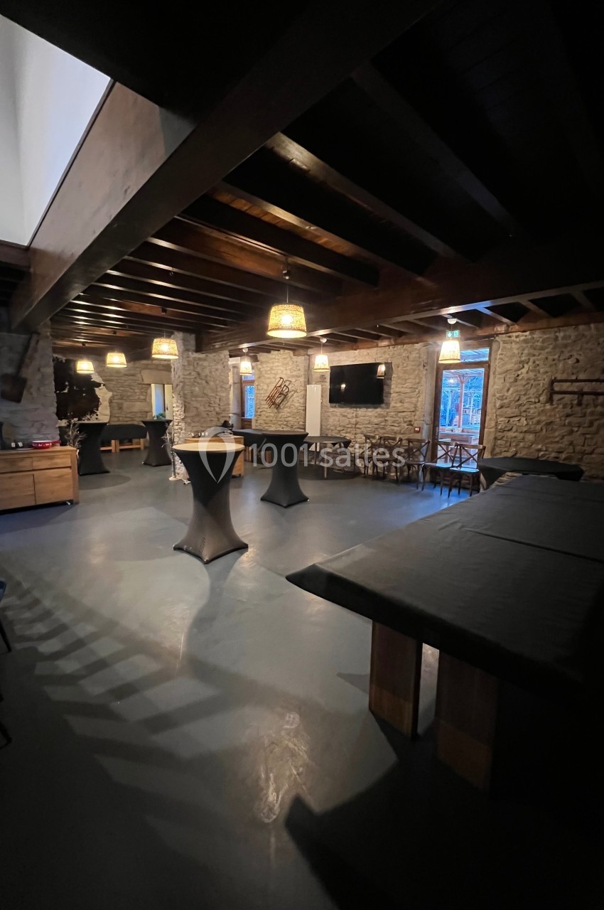 Salle intérieure avec murs en pierre, tables hautes, éclairage tamisé et grandes fenêtres donnant sur l'extérieur.