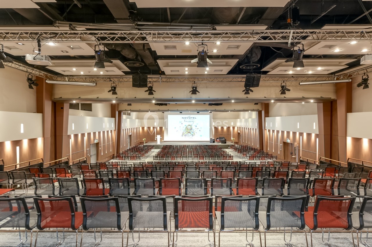 Salle de conférence vide avec des rangées de chaises et un écran de projection allumé au fond.