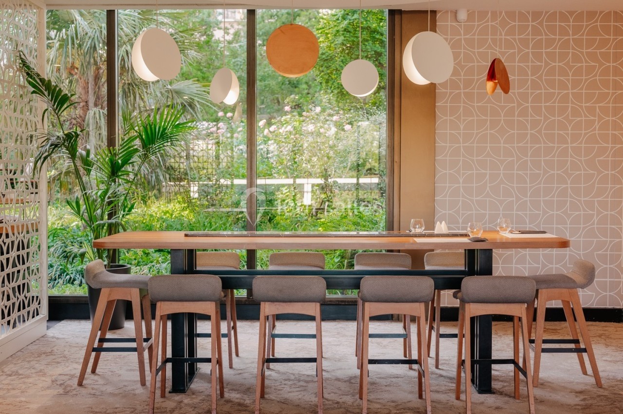 Salle à manger moderne avec une grande table en bois, des chaises rembourrées et vue sur un jardin verdoyant.