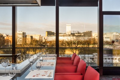 Vue de Paris à travers une fenêtre, montrant la Seine, un bâtiment moderne et l'horizon urbain avec des gratte-ciels.