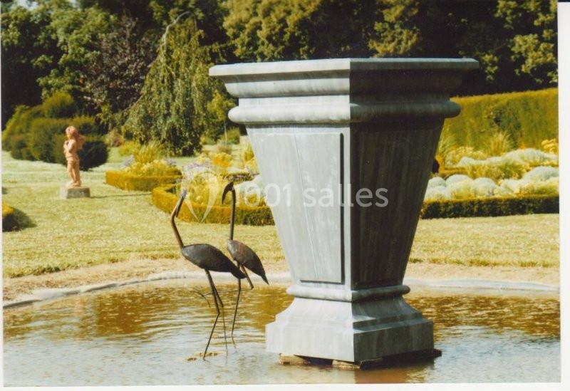Deux statues d'oiseaux dans un bassin près d'un grand vase en pierre, entourés de végétation et de sculptures de jardin.