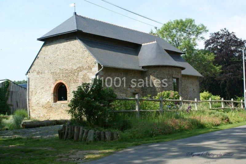 Bâtiment en pierre avec toit en ardoise, entouré de végétation et d'une clôture en bois, sous un ciel dégagé.