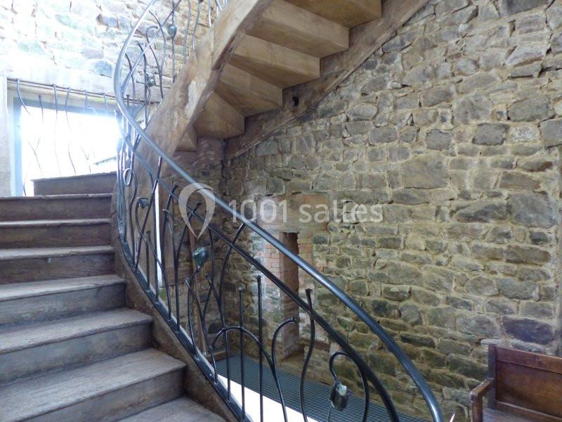 Escalier en bois avec rambarde en métal, situé dans un intérieur aux murs en pierre apparente.