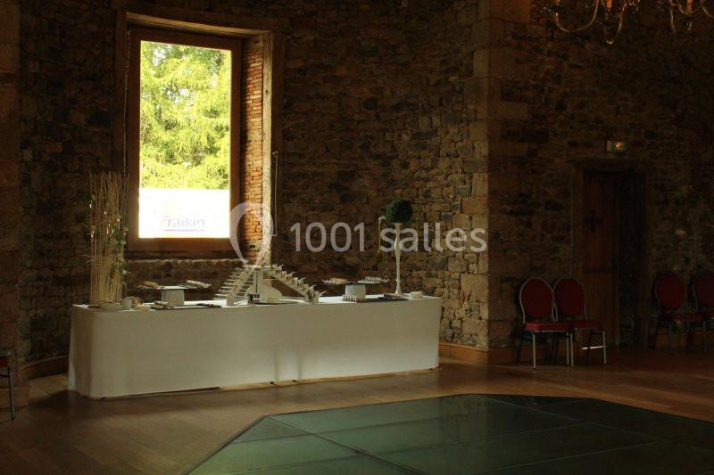 Table décorée avec des éléments modernes dans une salle en pierre, éclairée par une grande fenêtre donnant sur un jardin.