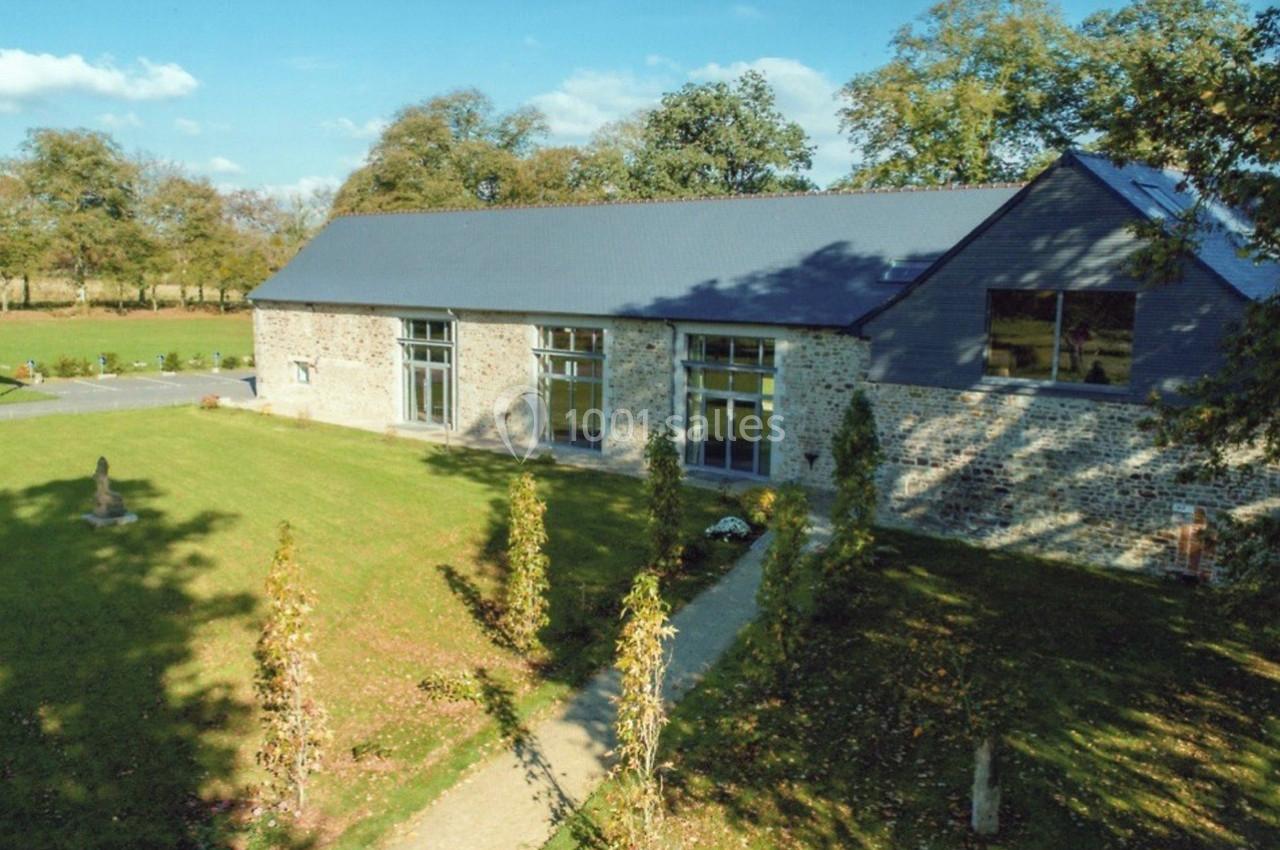 Bâtiment en pierre rénové avec toit en ardoise, grandes baies vitrées, entouré d'un jardin et d'arbres.