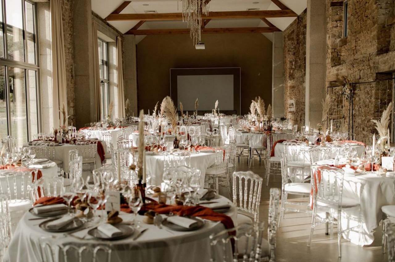 Salle de réception décorée pour un événement, avec des tables rondes dressées, nappes blanches et touches de rouge.