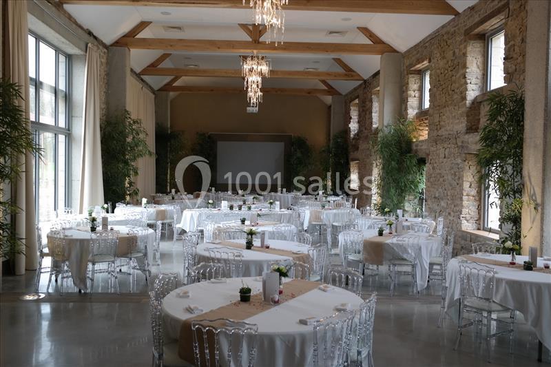 Salle de réception lumineuse avec tables rondes dressées, chaises transparentes et décorations végétales.