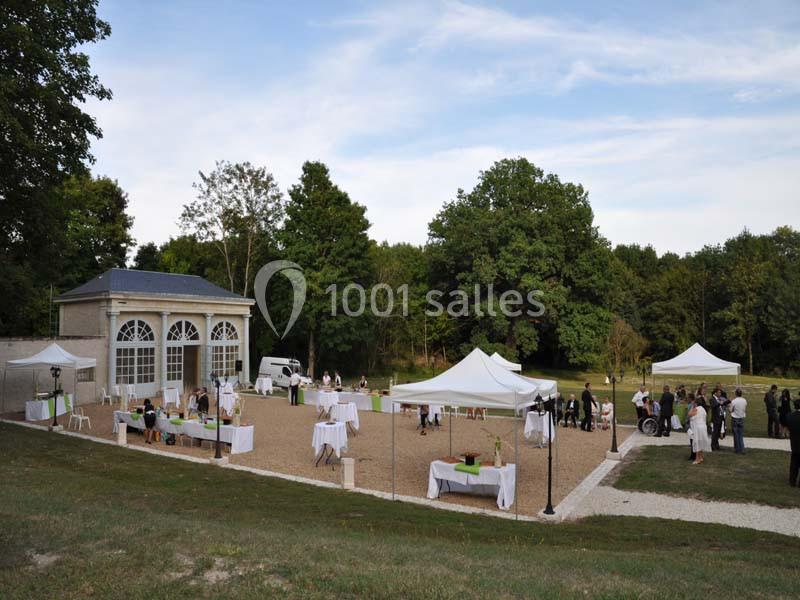 Jardin avec une orangerie, des tentes blanches et des invités debout lors d'un événement en plein air.
