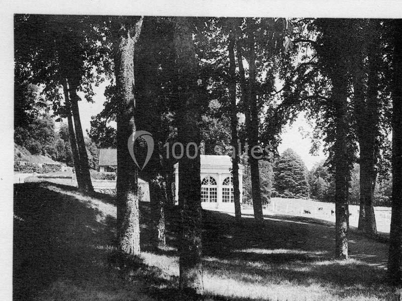 Vue en noir et blanc d'un parc arboré avec une structure vitrée en arrière-plan, entourée de pelouses et d'arbres.