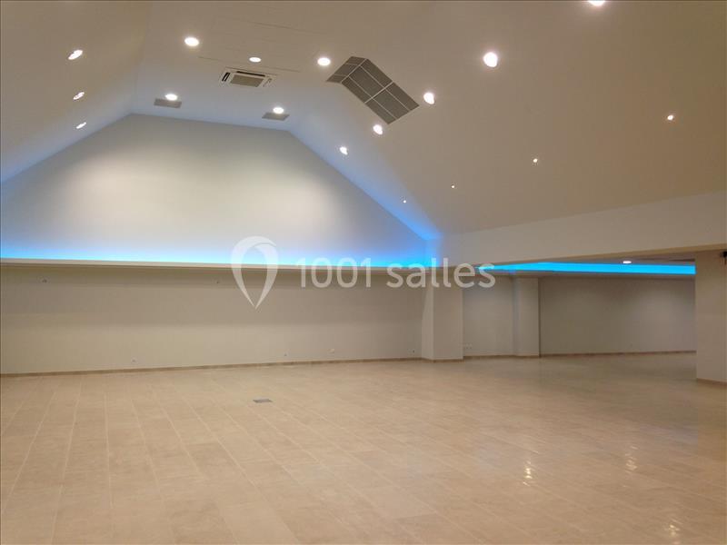 Salle spacieuse avec un plafond haut, éclairage LED bleu et sol carrelé beige.