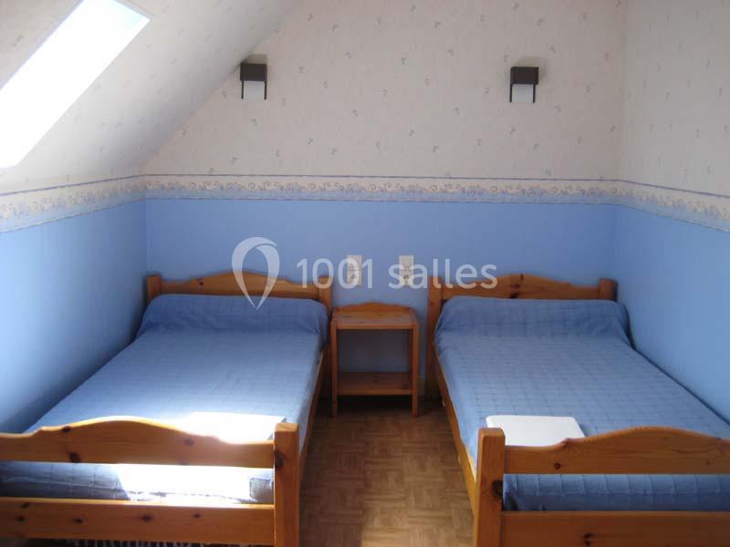 Deux lits simples en bois avec couvre-lits bleus dans une chambre mansardée aux murs bleus et parquet au sol.