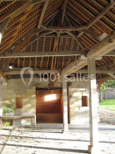 Charpente en bois apparente d'un bâtiment ancien avec murs en pierre et ouvertures laissant entrer la lumière naturelle.