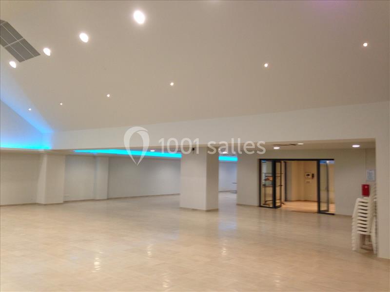 Salle spacieuse avec sol en carrelage clair, éclairage au plafond et bande lumineuse bleue sur les murs.