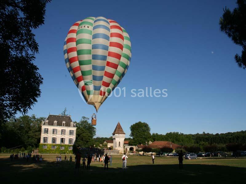Montgolfière colorée s'élevant dans le ciel au-dessus d'un parc avec une maison et des spectateurs au sol.