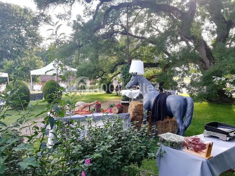 Cheval décoratif avec lampe sur la tête dans un jardin aménagé pour un événement, entouré de tables et de verdure.