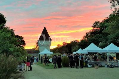 Vue aérienne de plusieurs bus stationnés près d'un bâtiment ancien, entourés de groupes de personnes et de verdure.