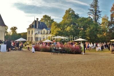 Vue aérienne de plusieurs bus stationnés près d'un bâtiment ancien, entourés de groupes de personnes et de verdure.