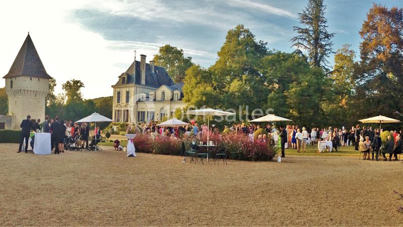 Groupe de personnes réunies dans un jardin devant un château, avec des parasols et des tables installés.