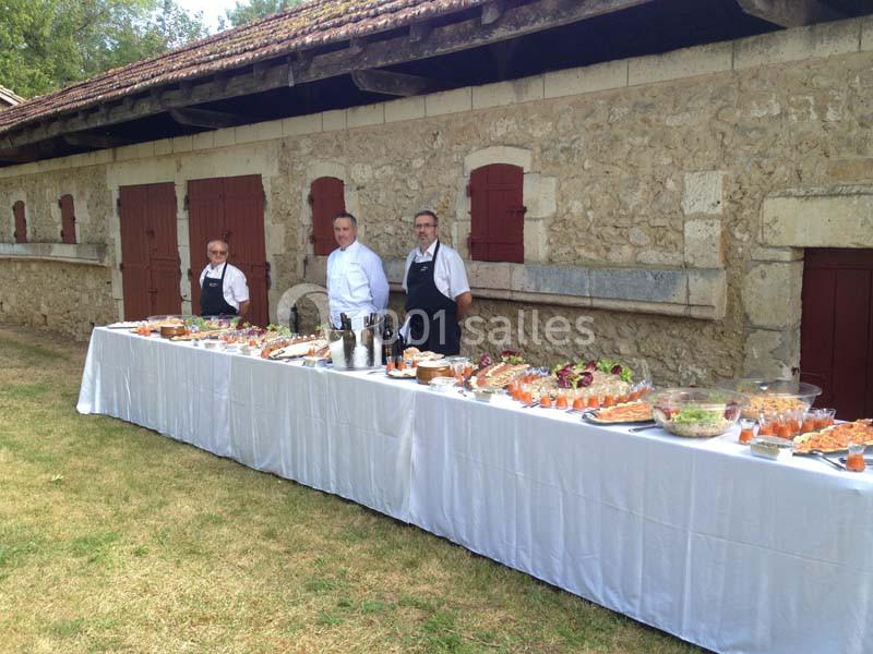 Trois chefs devant une longue table dressée avec des plats variés, située à l'extérieur près d'un bâtiment en pierre.