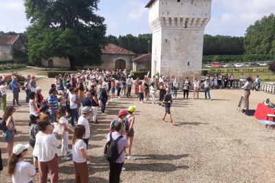 Vue aérienne de plusieurs bus stationnés près d'un bâtiment ancien, entourés de groupes de personnes et de verdure.