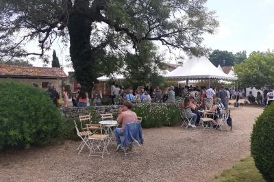 Vue aérienne de plusieurs bus stationnés près d'un bâtiment ancien, entourés de groupes de personnes et de verdure.