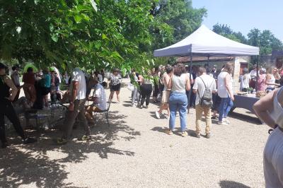 Vue aérienne de plusieurs bus stationnés près d'un bâtiment ancien, entourés de groupes de personnes et de verdure.