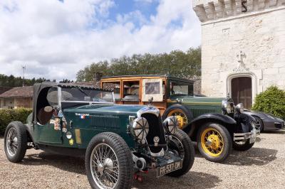 Vue aérienne de plusieurs bus stationnés près d'un bâtiment ancien, entourés de groupes de personnes et de verdure.