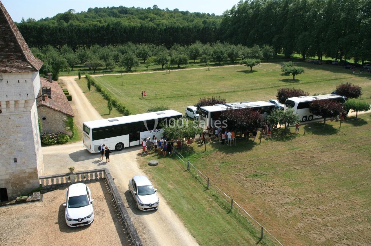 Vue aérienne de plusieurs bus stationnés près d'un bâtiment ancien, entourés de groupes de personnes et de verdure.