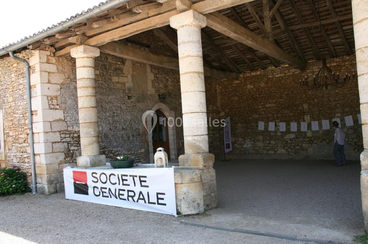 Entrée d'un bâtiment en pierre avec une bannière ’Société Générale’ accrochée sur un muret.