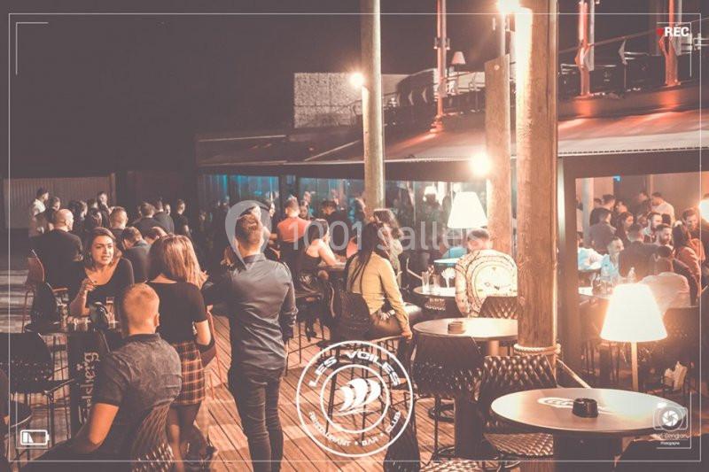 Personnes rassemblées dans un bar ou une terrasse animée en soirée, avec éclairage tamisé et ambiance conviviale.