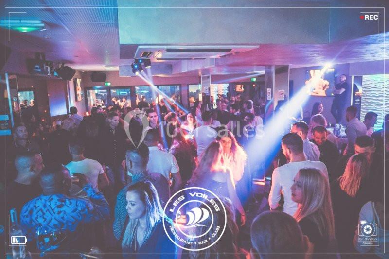 Foule de personnes dans une discothèque avec éclairages colorés et ambiance festive.