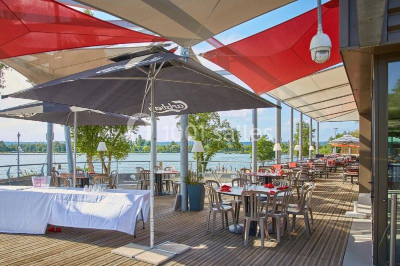 Terrasse d’un restaurant avec des tables dressées, des parasols colorés et vue sur un plan d’eau bordé de verdure.
