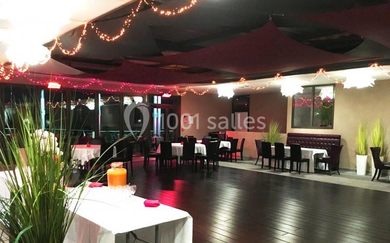 Salle de réception décorée avec des guirlandes lumineuses, tables dressées et plantes en pot.