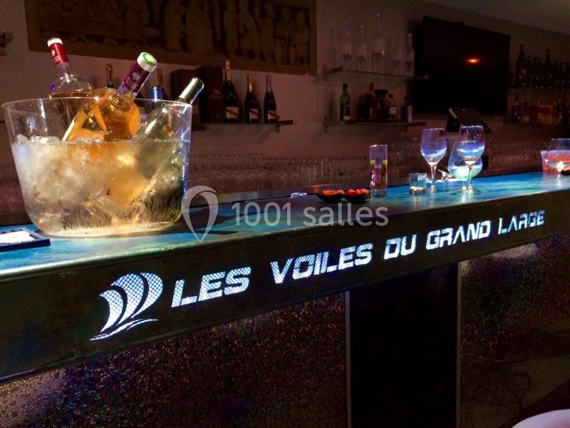 Seau à glace avec bouteilles et verres sur un comptoir lumineux marqué ’Les Voiles du Grand Large’.