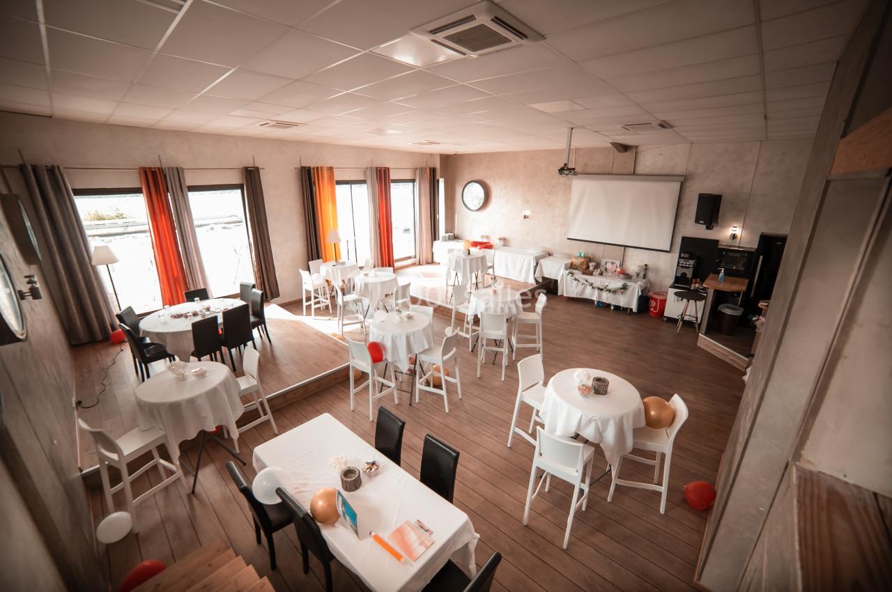 Salle de réception lumineuse avec tables rondes et rectangulaires dressées, décorée pour un événement.