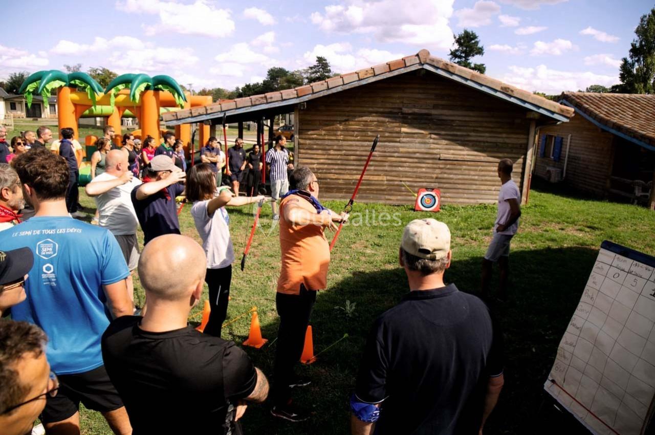 Des personnes participent à une activité de tir à l'arc en plein air, encadrées par un animateur devant une cible.