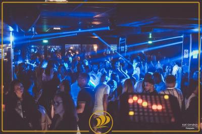 Foule dans une discothèque éclairée par des lumières bleues, avec une ambiance festive et un panneau lumineux au premier…