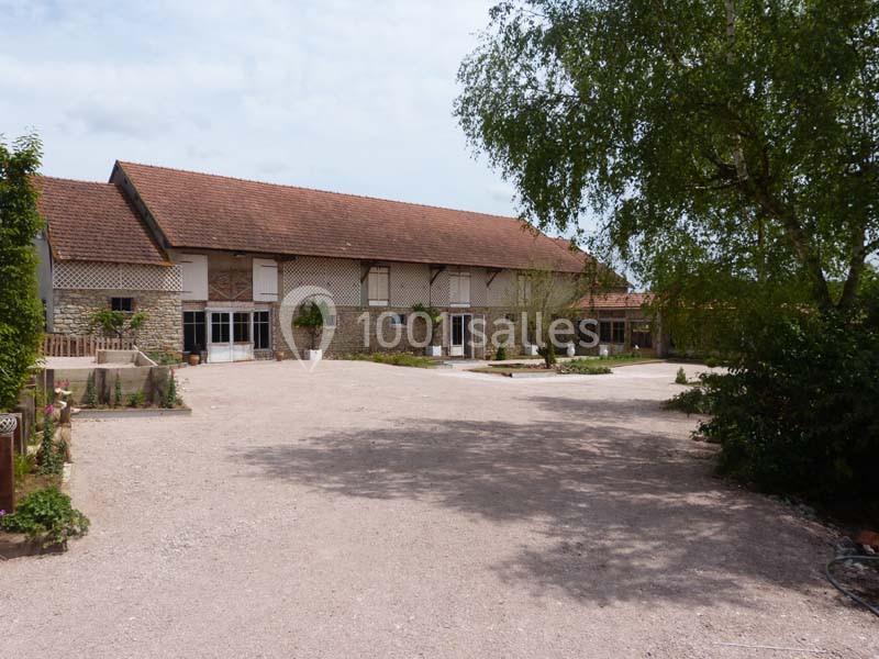 Cour devant un grand bâtiment en pierre avec toit en tuiles, entouré de végétation et d'aménagements extérieurs.