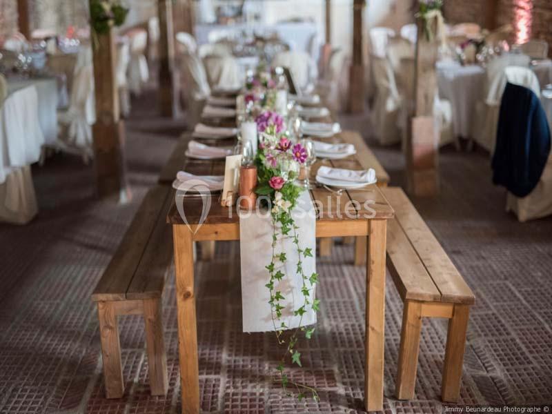 Table en bois décorée de fleurs et de feuillage, avec des bancs assortis, dans une salle de réception lumineuse.