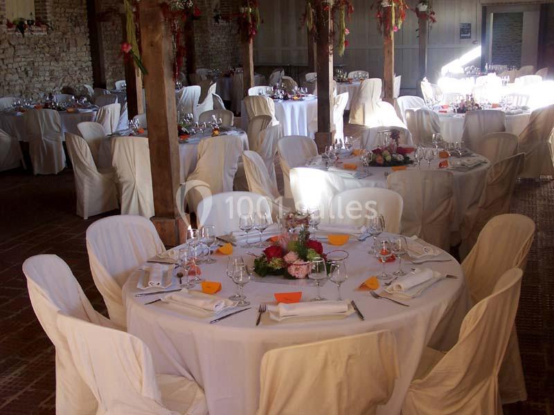 Salle de réception décorée avec des tables rondes dressées, nappes blanches et arrangements floraux colorés.