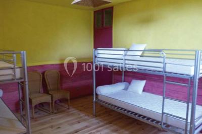 Dortoir sous combles avec murs en pierre, matelas au sol alignés et poutres apparentes.