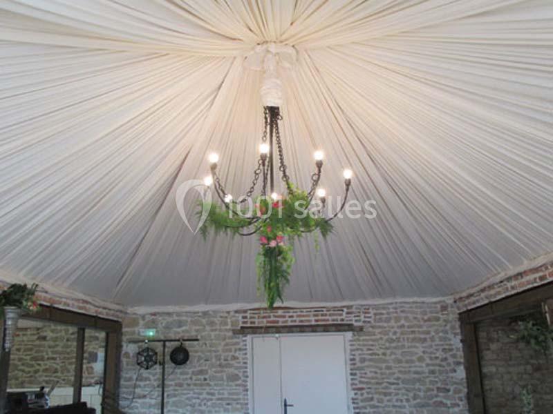 Plafond drapé en tissu blanc avec un lustre noir orné de feuillage et de fleurs suspendu au centre.