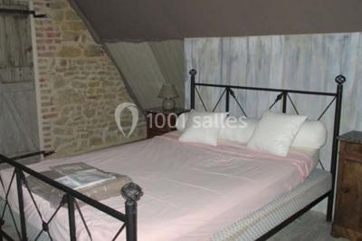 Dortoir sous combles avec murs en pierre, matelas au sol alignés et poutres apparentes.