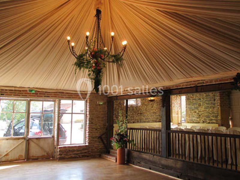 Salle de réception avec plafond drapé, lustre décoré de fleurs, murs en pierre et grandes fenêtres vitrées.
