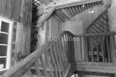 Dortoir sous combles avec murs en pierre, matelas au sol alignés et poutres apparentes.