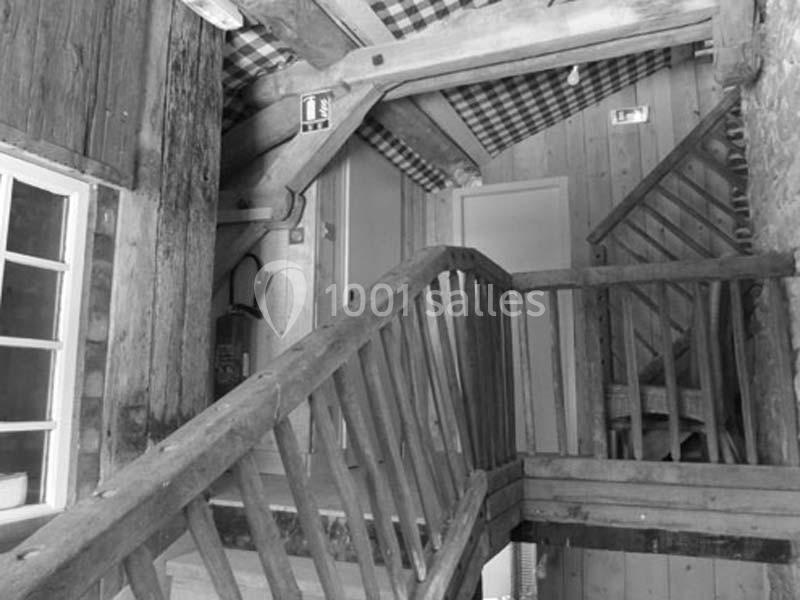 Escalier en bois rustique dans un intérieur avec poutres apparentes et plafond décoré de tissu à carreaux.