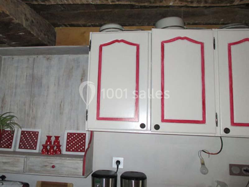 Placards de cuisine blancs avec bordures rouges, étagère assortie en dessous et poutres en bois visibles au plafond.