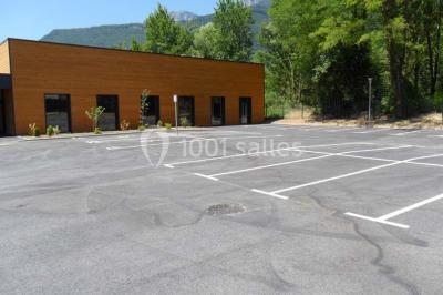 Parking vide avec marquages au sol, situé devant un bâtiment en bois entouré d'arbres et de montagnes.