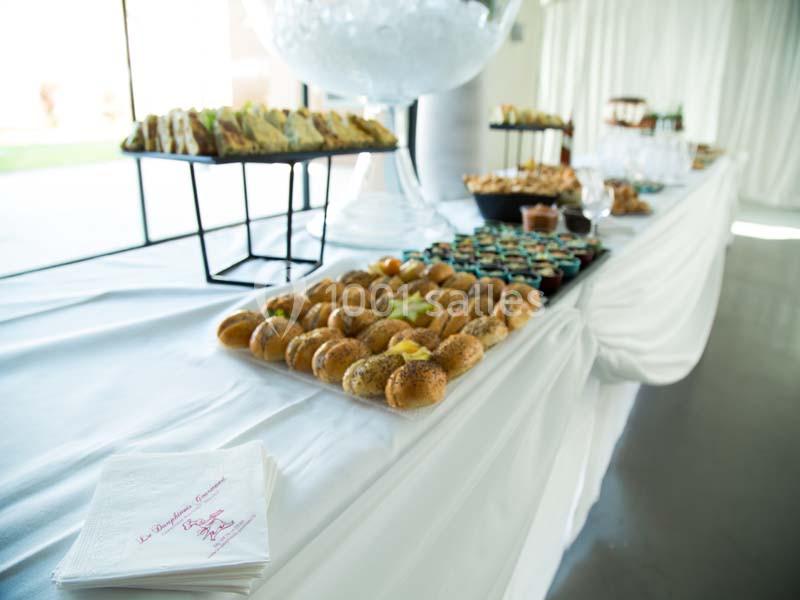 Buffet avec des plateaux de petits sandwichs, verrines et desserts disposés sur une table blanche drapée.